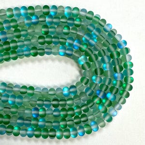May include: A strand of round, iridescent glass beads in shades of green and blue. The beads have a frosted finish and are approximately 6mm in diameter.