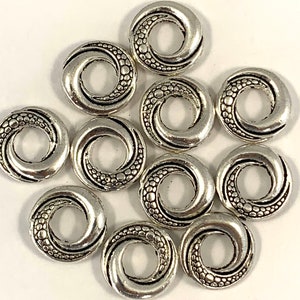 May include: Ten silver-toned metal spacer beads with a swirl design. Each bead has a small hole in the center.
