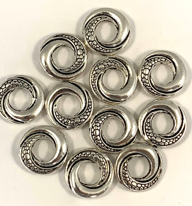 May include: Ten silver-toned metal spacer beads with a swirl design. Each bead has a small hole in the center.