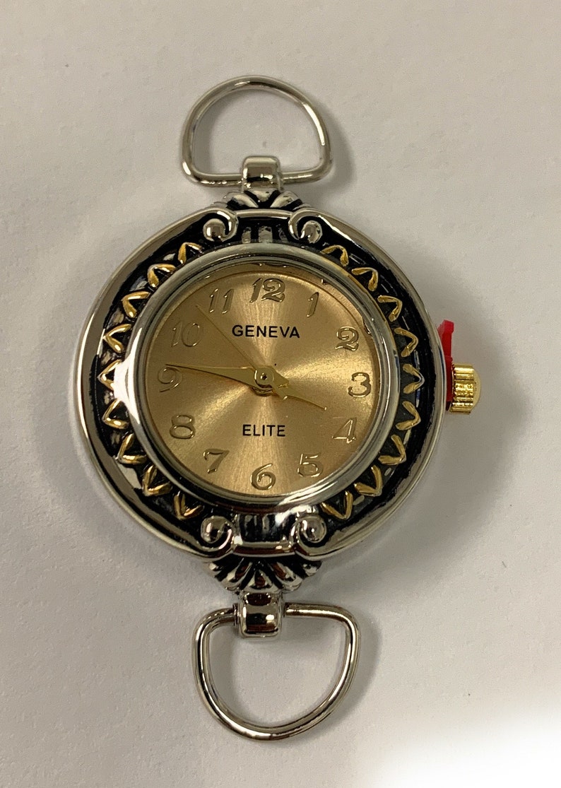 May include: A silver and gold tone wristwatch with a round face and a decorative border. The face is gold with black hands and black Roman numeral markings. The watch face says "GENEVA" and "ELITE".