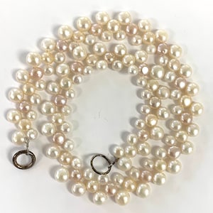 May include: A triple strand pearl necklace with a silver clasp. The pearls are white and cream colored and are of varying sizes.