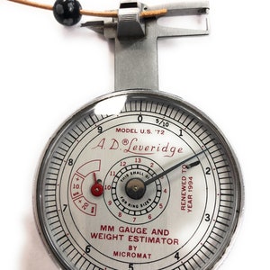 May include: A silver ring gauge and weight estimator by Micromat. The gauge is marked with millimeters and has a small dial that reads "This small dial for ring sizes". The gauge is labeled "Model U.S. '72" and "A.D. Leveridge".