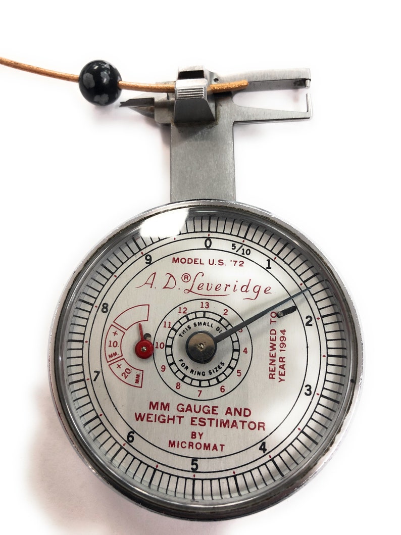 May include: A silver ring gauge and weight estimator by Micromat. The gauge is marked with millimeters and has a small dial that reads "This small dial for ring sizes". The gauge is labeled "Model U.S. '72" and "A.D. Leveridge".