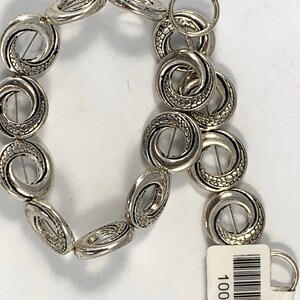 May include: Silver tone metal beads with a textured swirl design. The beads are strung together to form a bracelet or necklace.