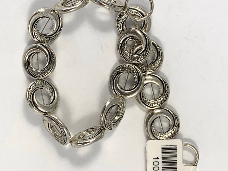 May include: Silver tone metal beads with a textured swirl design. The beads are strung together to form a bracelet or necklace.