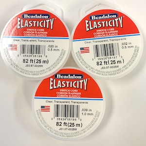 May include: Three spools of clear Beadalon Elasticity stretch cord, each with a red label and white text. The labels state "Beadalon Elasticity Stretch Cord Cordon Elastique Cordon Elastico" and "Clear, Transparent, Transparente". Each spool contains 82 feet (25 meters) of cord and has a different thickness: 0.020 inches (0.5 mm), 0.032 inches (0.8 mm), and 0.039 inches (1.0 mm).