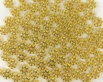 May include: A large quantity of gold-colored metal beads with a flower-shaped design. Each bead has a small hole in the center.
