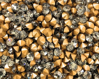 May include: A close-up image of a large quantity of small, round, gold and black rhinestones. The rhinestones are arranged in a random pattern and are all the same size.