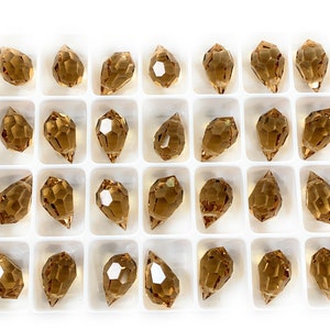 K&ouml;nnte beinhalten: Eine Schale mit 36 bernsteinfarbenen Glasperlen in Tropfenform. Die Perlen sind in einem wei&szlig;en Kunststofftablett in einem Raster angeordnet.