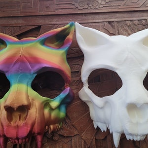 K&ouml;nnte beinhalten: Zwei Tier Sch&auml;del Masken, eine in Regenbogenfarben bemalt und die andere in Wei&szlig;.