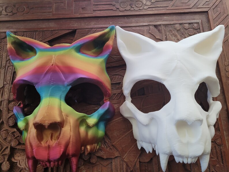 K&ouml;nnte beinhalten: Zwei Tier Sch&auml;del Masken, eine in Regenbogenfarben bemalt und die andere in Wei&szlig;.