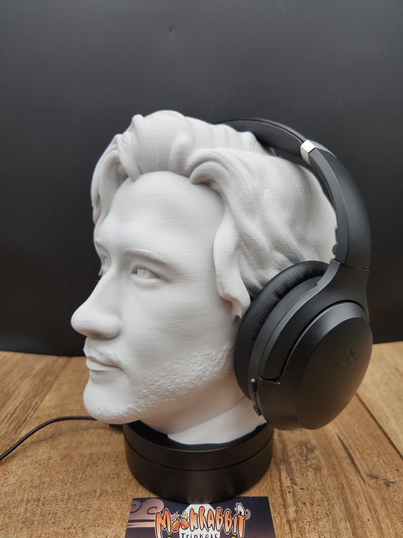 May include: A white bust of a man with a beard and headphones. The bust is on a black base, and the headphones are black. The bust is made of a light-colored material, and the headphones are resting on the bust's head.