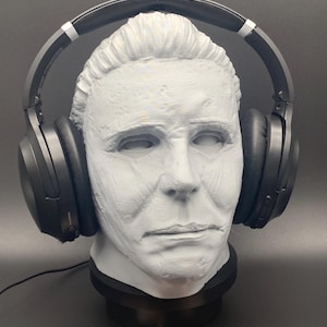 May include: A gray bust of a character with black headphones. The bust is mounted on a black base. Two business cards with the text "Moonrabbit Trinkets" are at the base.