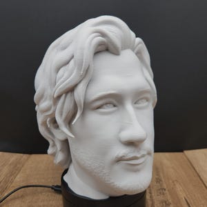 May include: A white bust of a man with long hair and a beard, mounted on a black base. The bust is a detailed sculpture, showcasing facial features. A business card with the text "Mr. Krabbit Trinkets" is visible.