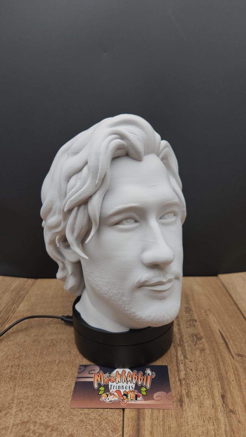 May include: A white bust of a man with long hair and a beard, mounted on a black base. The bust is a detailed sculpture, showcasing facial features. A business card with the text "Mr. Krabbit Trinkets" is visible.