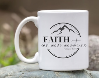May include: White ceramic mug with a curved handle. The mug features a black graphic of a mountain range inside a circle, with the words "FAITH can move mountains" and "Matthew 17:20" in black text.