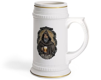 Op de afbeelding: Witte keramische bierpul met een handvat en gouden rand. De pul heeft een omlijste illustratie van een bebaarde man in een gehuurde mantel die een bierpul vasthoudt. Het ontwerp is in tinten bruin, beige en goud.