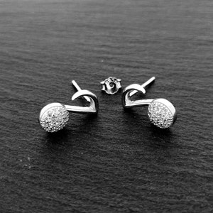 Peut inclure: Une paire de boucles d'oreilles en argent avec un petit motif rond en cristal. Les boucles d'oreilles ont une forme incurvée et un fermoir à tige.