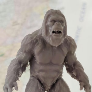 Könnte beinhalten: Graue, detaillierte Figur einer gorillaähnlichen Kreatur, möglicherweise Bigfoot. Die Figur hat einen muskulösen Körperbau, mit sichtbarer Fellstruktur und offenem Mund. Sie steht aufrecht, mit Armen an den Seiten, und ist wahrscheinlich ein Sammlerstück oder Spielzeug.