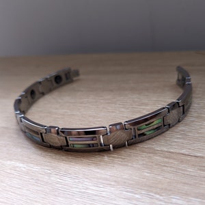 以下が含まれることがあります： 黒と緑のアワビの貝殻の象嵌が施された銀色の磁気ブレスレット
