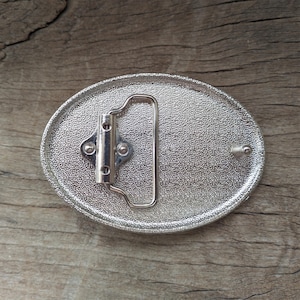 May include: Silver oval belt buckle with a textured surface and a silver metal buckle.