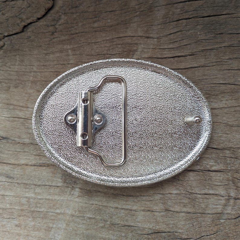 May include: Silver oval belt buckle with a textured surface and a silver metal buckle.