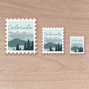 May include: Three postage stamp-style stickers with a Colorado landscape design. The stickers feature a mountain range, trees, and the word "Colorado" in a script font. The color palette includes shades of blue, green, and white.