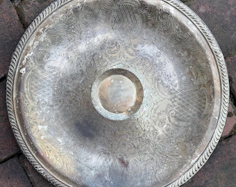 May include: A silver serving tray with an ornate, embossed design. The tray has a raised center section and a scalloped edge.