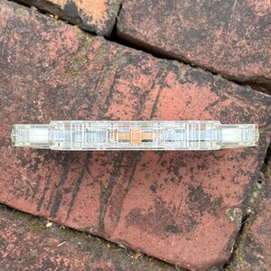 May include: A clear cassette tape with a visible magnetic tape reel. The cassette is resting on a weathered brick surface. The tape's transparent casing allows a view of the internal components, including the tape spools and the magnetic tape itself.