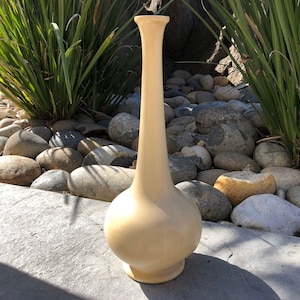 Può includere: Un vaso in ceramica di colore crema, alto e sottile, con una base rotonda e bulbosa e un collo lungo e sottile.