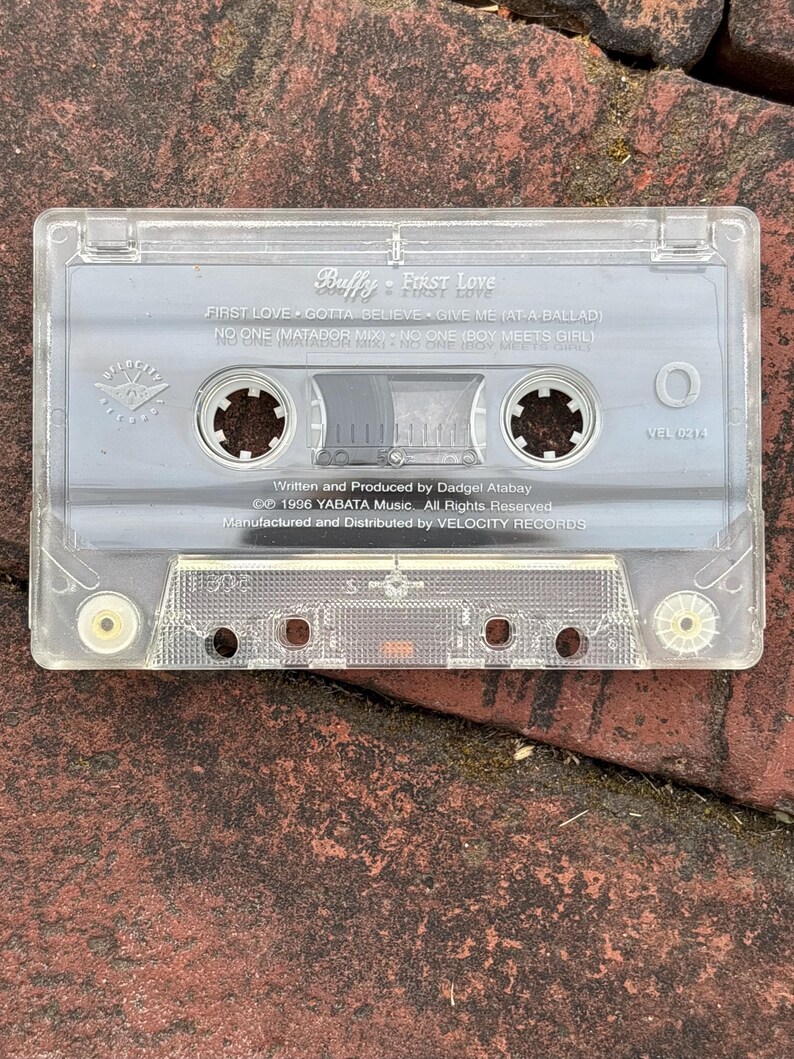May include: A clear cassette tape labeled "Buffy - First Love." The tape includes song titles like "First Love" and "No One." The cassette is marked with "Velocity Records" and the year 1996.