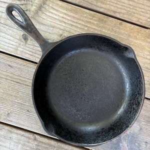 May include: A black cast iron skillet with a loop handle. The skillet is seasoned and has a rough, textured surface.