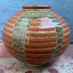 May include: A small, round ceramic vase with a textured, striped pattern in shades of brown, orange, and white.