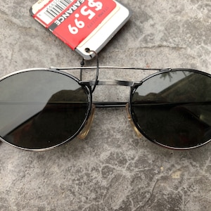 May include: A pair of round, black sunglasses with a silver metal frame. The sunglasses have a dark lens and are made in Taiwan.