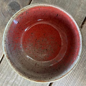 May include: A red ceramic bowl with a speckled glaze. The bowl has a white rim and a slightly textured surface.