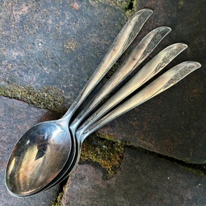 Könnte beinhalten: Vier silberne Löffel mit floralen Mustern auf den Griffen sind übereinander gestapelt.