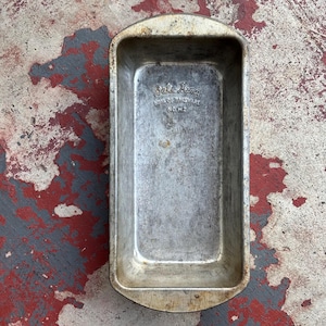 May include: Vintage Bake King loaf pan made of silver-colored metal. The rectangular pan has rounded edges and the text "Bake King" and "NO. H2" are embossed on the interior. The pan shows signs of wear and tear, with a distressed appearance.