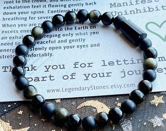 May include: A black beaded bracelet with a mix of matte and polished beads, including a cylindrical black stone. The bracelet is displayed on a card with text and a website address.
