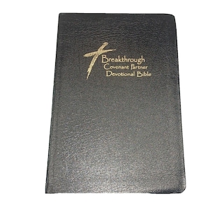 May include: A black, textured, hardcover book titled Breakthrough Covenant Partner Devotional Bible. The cover features a gold-colored cross graphic and gold lettering that reads Breakthrough Covenant Partner Devotional Bible.