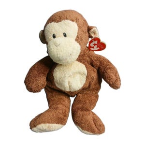 May include: A brown and cream-colored plush monkey toy with a soft, textured fabric finish. The stuffed animal features a round face, a light-colored belly patch, and a heart-shaped red Ty Puffies tag attached to its right ear.