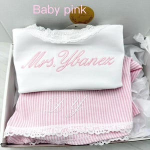 May include: A white tank top with lace trim and the embroidered text Mrs. Ybanez in baby pink thread, paired with a pink and white striped garment featuring white lace trim and the embroidered initials DY in white thread.