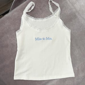 May include: White camisole with lace trim and straps. The text "Miss to Mrs." is embroidered in light blue on the front. This bridal-themed top is perfect for a hen party or wedding day.