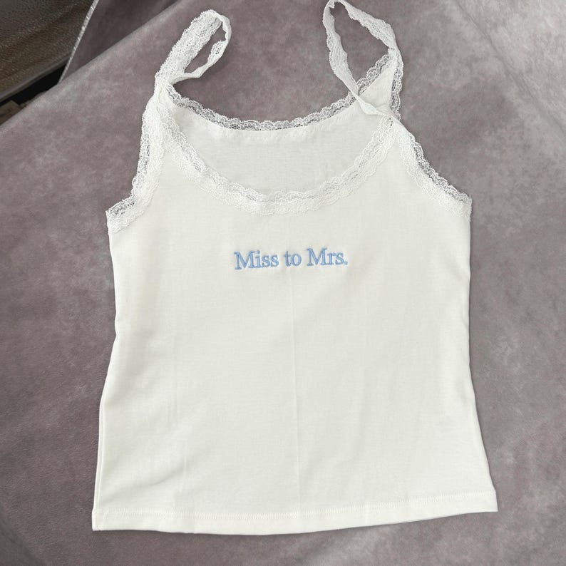 May include: White camisole with lace trim and straps. The text "Miss to Mrs." is embroidered in light blue on the front. This bridal-themed top is perfect for a hen party or wedding day.