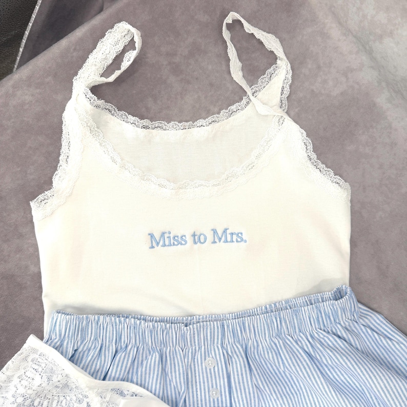 May include: A white camisole with lace detailing and blue striped shorts. The camisole features the embroidered text "Miss to Mrs." in blue. The shorts have a button closure and elasticated waistband.