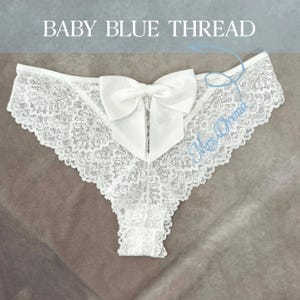 May include: White lace underwear featuring a large satin bow. The underwear has a delicate floral lace pattern and a scalloped edge. The text "BABY BLUE THREAD" is at the top of the image.
