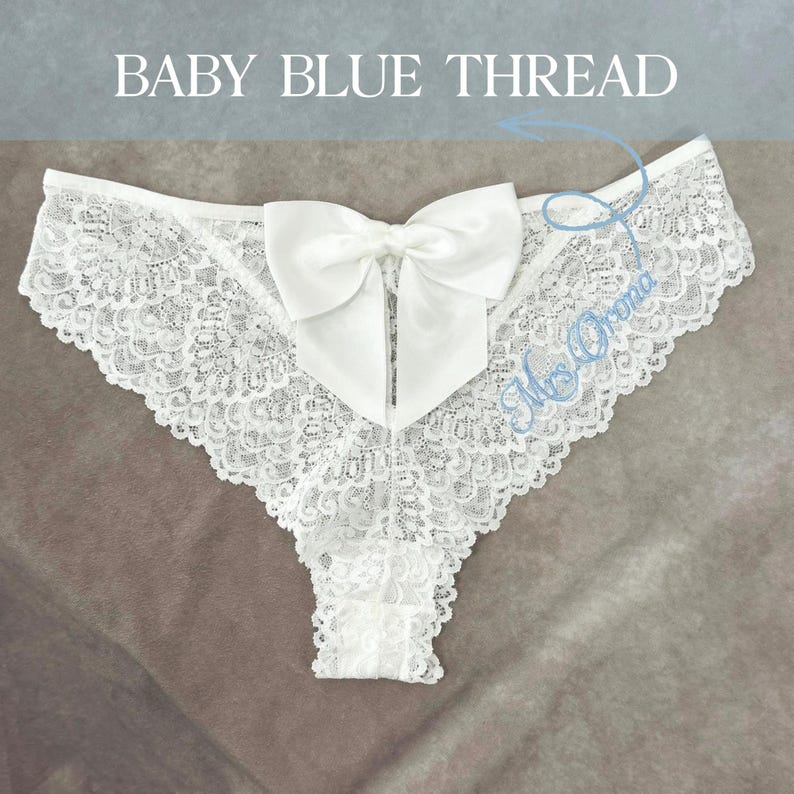 May include: White lace underwear featuring a large satin bow. The underwear has a delicate floral lace pattern and a scalloped edge. The text "BABY BLUE THREAD" is at the top of the image.