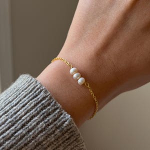 Peut inclure: Un bracelet en or délicat orné de trois perles blanches. Le bracelet est composé d'une fine chaîne en or et se porte au poignet. Les perles sont espacées de manière uniforme et ajoutent une touche d'élégance au bijou.