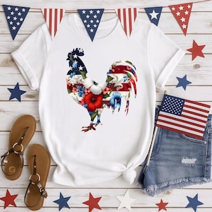May include: White t-shirt featuring a rooster design filled with floral and American flag patterns. The shirt is styled with denim shorts, sandals, and patriotic decorations, including a small American flag and star-shaped ornaments.