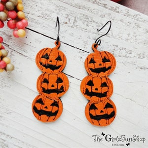 May include: A pair of orange wooden earrings shaped like stacked jack-o'-lantern faces. The earrings have black wire hooks.