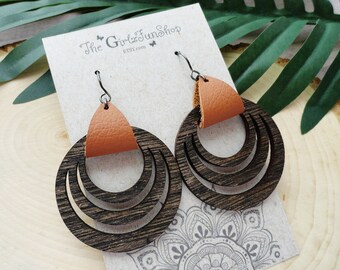 May include: A pair of brown wooden earrings with a layered circle design and a small orange leather accent. The earrings are hanging on a white card with the text "The Girlz Junkshop ETSY.com".